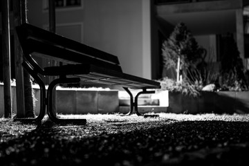 A black and white image of a backlit bench from a low perspective at night
