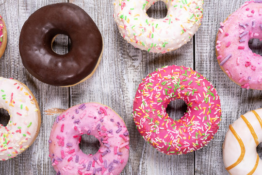 Traditional doughnuts with multicolored glaze laid out on white painted wooden background. Top view, flat lay, close-up.