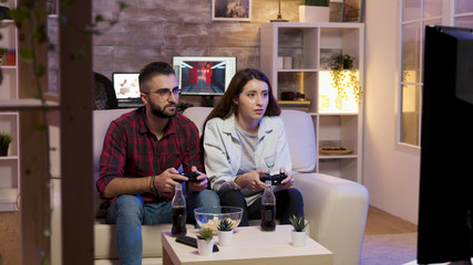 Cheerful young couple sitting on couch and playing video games