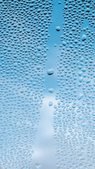 Drops water on window for mobile wallpaper design. Blue cloudy sky backdrop. Spotted abstract texture background. Spring wet weather. Droplets on glass in vertical natural cover. Fit to autumn
