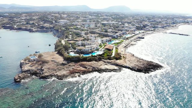Aerial shot of Crete shore, view on Sarantaris cape and Anissaras at sunny day. Stony shore on headland, sandy beaches seen on right. Many buildings on land, hotels and apartments