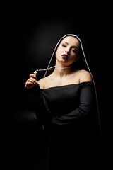 sexy young nun in black dress holding cross, isolated on black