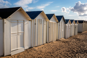 Obraz premium Row of white wooden beach huts or cabins alongside Riva Bella beach on early evening, Ouistreham, Normandy, France.