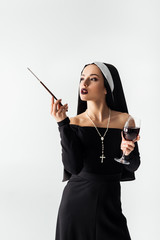 attractive nun with glass of wine smoking a cigarette in mouthpiece isolated on grey