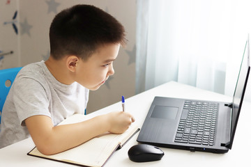 a small boy Samir is sitting at a table playing on the computer and phone