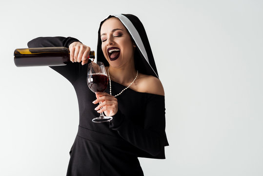 excited sexy nun pouring wine from bottle into glass isolated on grey