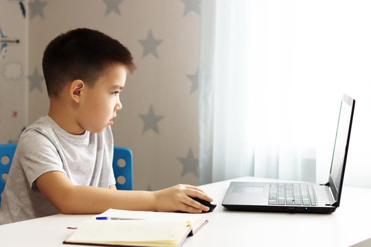 A Small Boy Samir Is Sitting At A Table Playing On The Computer And Phone