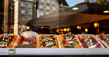 Assorted mouth-watering Belgian waffles in a shop window. Panorama format.