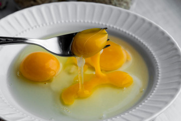Three broken eggs on the white porcelain plate.Preparing to cook omelette.One yolk on fork holding.