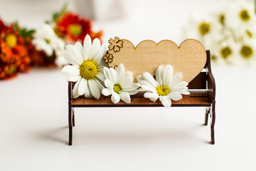 Mini wooden bench and empty wooden heart label on it with beautiful white daisies.Conceptual image of special days.