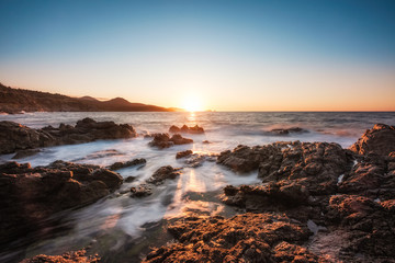 Waves washing onto rocky Corsica coastline at sunset