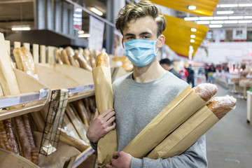 Young man wearing disposable medical mask shopping in supermarket during coronavirus