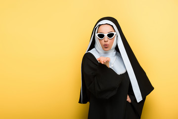 attractive nun in sunglasses blowing air kiss on yellow