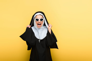 attractive excited nun in sunglasses on yellow