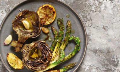 artichoke and asparagus grill. Tasty vegetables are first cooked for a couple, then fried on a grill, poured with olive oil and spices. spring vegetables. background concrete. top view.  copy space. 