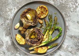 artichoke and asparagus grill. Tasty vegetables are first cooked for a couple, then fried on a grill, poured with olive oil and spices. spring vegetables. background concrete. top view.  copy space. 