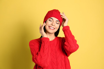 Young woman wearing warm sweater and hat on yellow background. Winter season