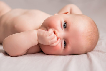 Happy 3 months old baby smiling, lying on white bed