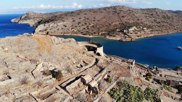 Fortifications and buildings remains at Spinalonga fort, aerial orbiting shot. Stone walls and redoubt remains at top of hill, historical site and popular tourist attraction at North-East Crete island