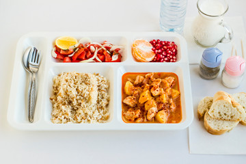 Traditional Turkish Meal with chicken potato,rice,tomato salad and fruits in the white portion food tray.Table d'hote-known TABLDOT in TR-Designed on the white surface.