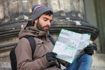 Tourist man sitting on stairs looking at map of the most famous places in the city