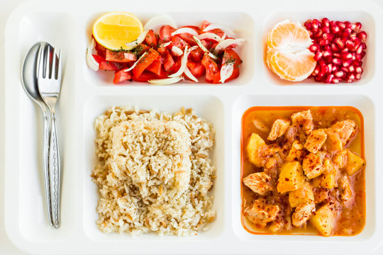 Traditional Turkish Meal with chicken potato,rice,tomato salad and fruits in the white portion food tray.Table d'hote-known TABLDOT in TR-Designed on the white surface.