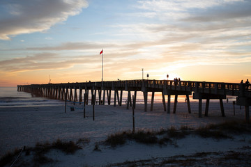 Obraz premium sunset at panama city beach pier with sun going down behind pier and beautiful clouds and sky and ocean