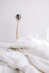 A young girl holds a cup of coffee on an outstretched hand in bed