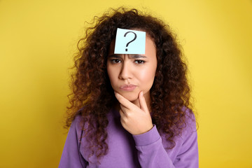 Emotional African-American woman with question mark sticker on forehead against yellow background