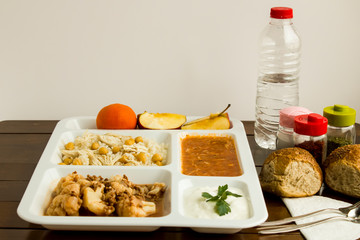 White food tray (table d'hote) with traditional Turkish meals and a bottle of water on wooden table, top view