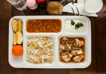 White food tray (table d'hote) with traditional Turkish meals and a bottle of water on wooden table, top view