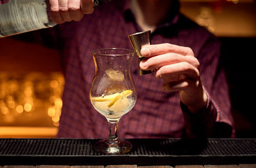 At the nightclub, the bartender is preparing an alcoholic cocktail filling the jigger with alcohol.