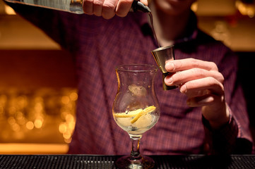 The bartender makes a cocktail in a nightclub. Uses a jigger for dosing.
