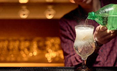 An experienced bartender adds lemon water with gases to a cocktail glass.