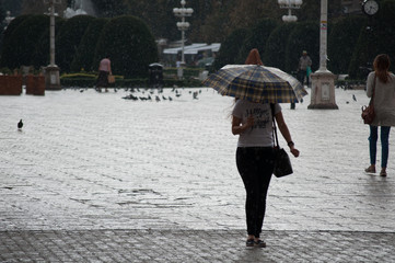 Woman walking on the street and holding an umbrella. Real people.