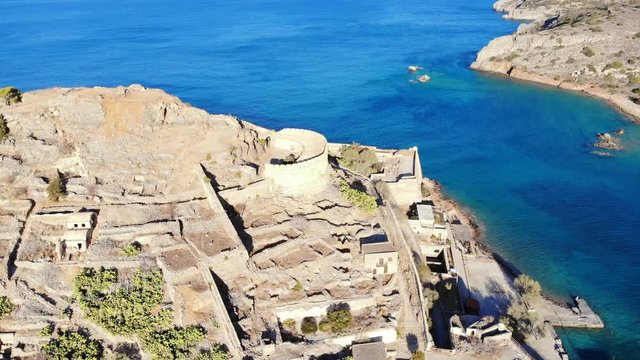 Former military defence structures on hill at Spinalonga fortress isle, rounded tower remains on top point, aerial shot. Popular tourist attraction of Crete Island