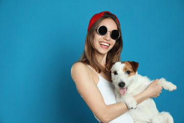 Young woman with her cute Jack Russell Terrier on light blue background, space for text. Lovely pet