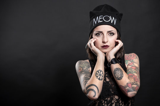 Ragazza  tatuata con cuffietta indossa una canotta nera ,e posa con aria seria  isolata su sfondo nero