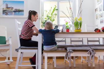 Junge Mutter arbeit im Home Office und passt auf ihr kleines Kind auf, corona covid 19