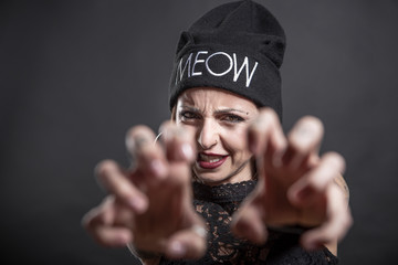 Ragazza  tatuata con cuffietta con scritta Meow simula il gatto con le mani e la faccia  , isolata su sfondo nero © alex.pin