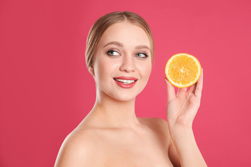 Young woman with cut orange on pink background. Vitamin rich food
