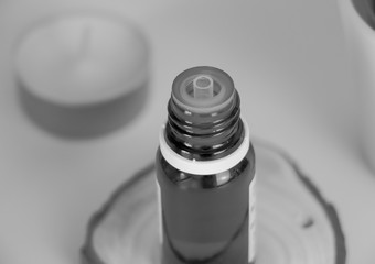 Frasco de aceite esencial cerrado sobre tronco y vela al fondo en blanco y negro