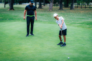 Golf Putting Training. Golf Instructor with Young Boy Practicing on the Putting Green