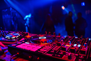 DJ console for mixing music with blurry people dancing at a nightclub party