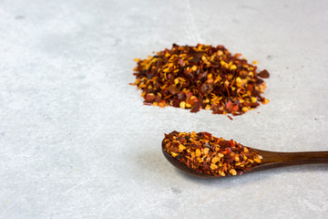 Dried crushed chilli pepper in a spoon and slide on the table on a gray background.