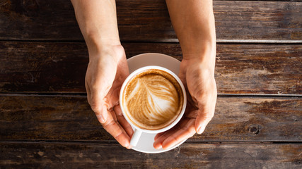 hand holding late coffee cup, round and white coffee cup on wooden table