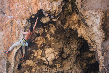 A strong man climbs a beautiful orange rock.