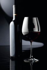 Glass and bottle of red wine on a black background.