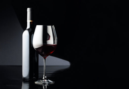 Glass and bottle of red wine on a black background.