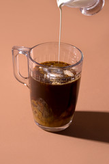 black coffee in a cup in which milk or cream is poured on a brown background